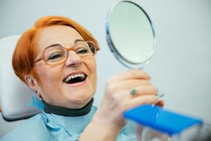 An older woman admiring her new dentures with a hand mirror