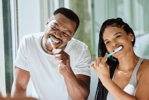 Couple smiling while brushing teeth together